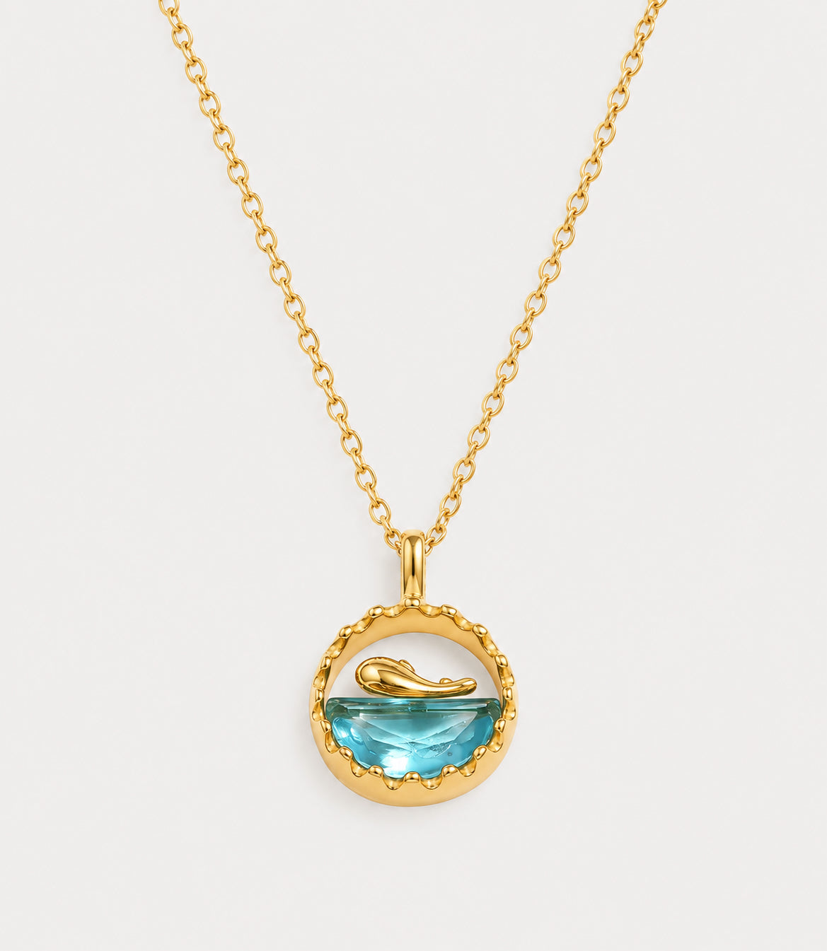 Gold plated necklace with a round pendant holding a blue topaz style stone and a small gold whale tail on a dainty cable chain